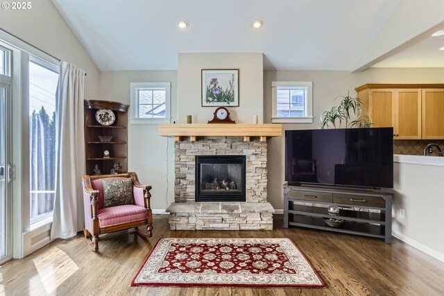 living area with vaulted ceiling, a stone fireplace, wood finished floors, and recessed lighting