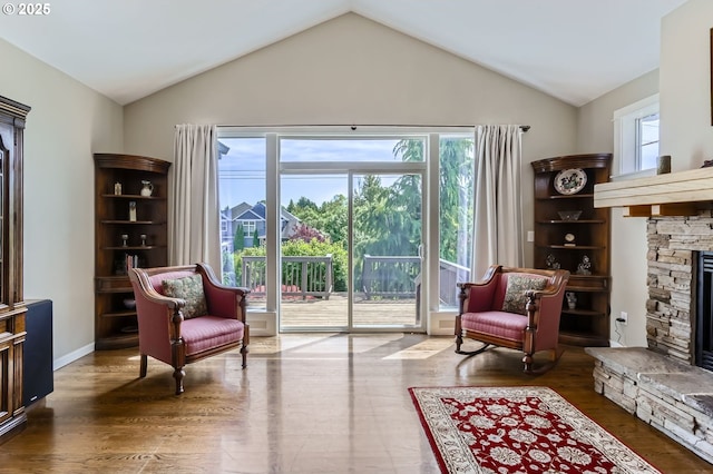 sitting room featuring a stone fireplace, healthy amount of natural light, lofted ceiling, and wood finished floors
