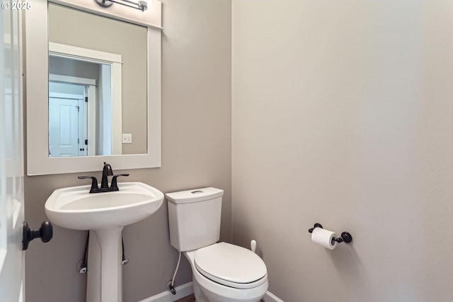 half bathroom featuring toilet, baseboards, and a sink