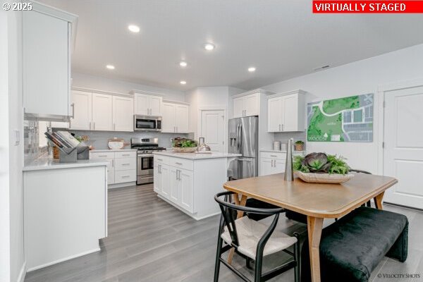 2747 Woodfern Ter Lot 57, Eugene, OR 97403 - kitchen featuring appliances with stainless steel finishes, light countertops, white cabinets, light wood-style floors, and a kitchen island with sink