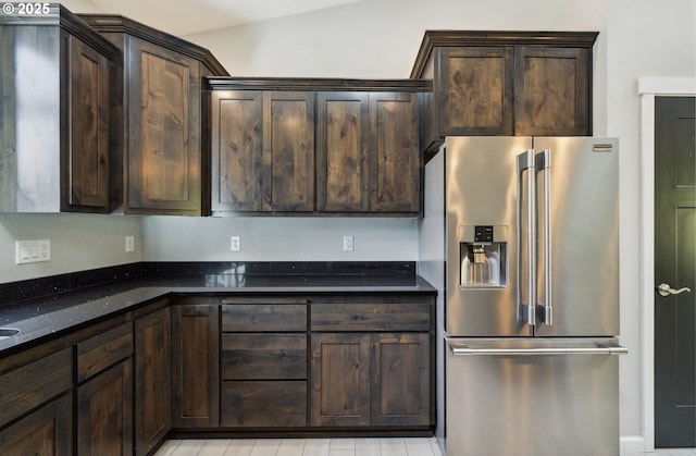 kitchen featuring stainless steel refrigerator with ice dispenser, dark brown cabinets, and dark stone countertops