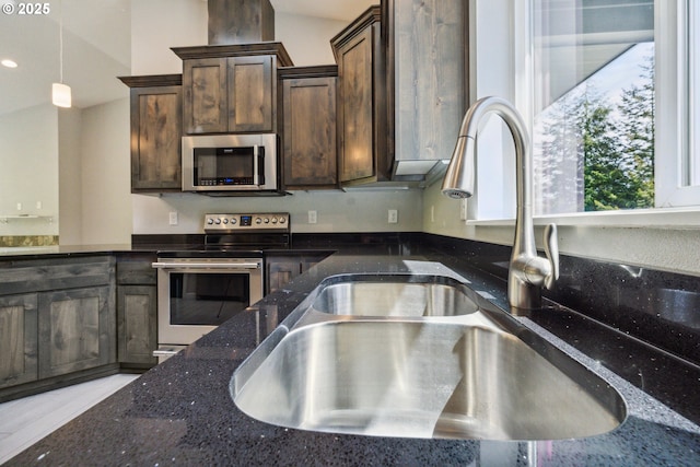 kitchen featuring stainless steel appliances, a sink, dark brown cabinetry, dark stone counters, and pendant lighting