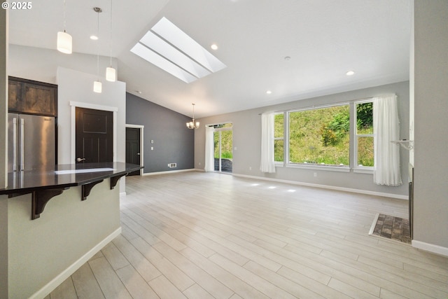 unfurnished living room featuring lofted ceiling, baseboards, a skylight, light wood-style floors, and a chandelier