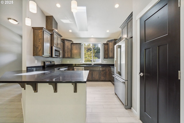 kitchen with appliances with stainless steel finishes, a peninsula, a kitchen bar, dark brown cabinetry, and decorative light fixtures
