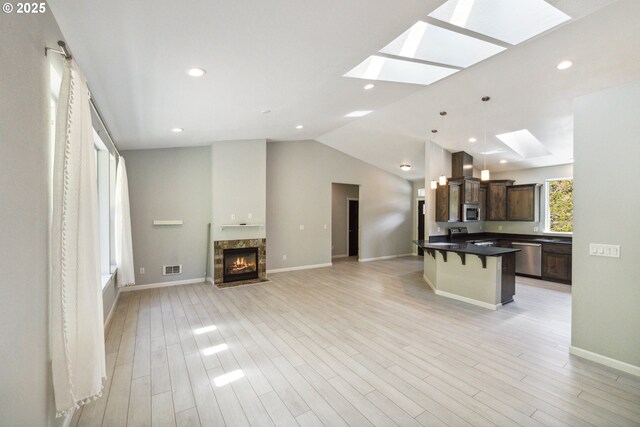 kitchen featuring a skylight, a breakfast bar, stainless steel appliances, dark brown cabinetry, and dark countertops
