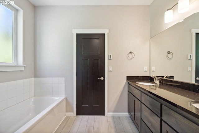 bathroom featuring a bath, wood finished floors, double vanity, and baseboards