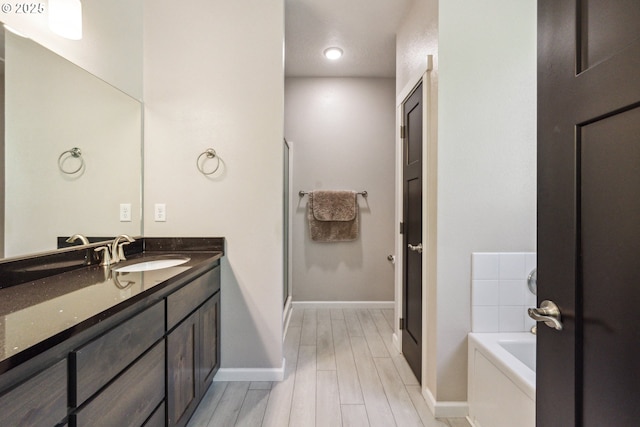 full bathroom featuring vanity, wood finished floors, a garden tub, baseboards, and a shower