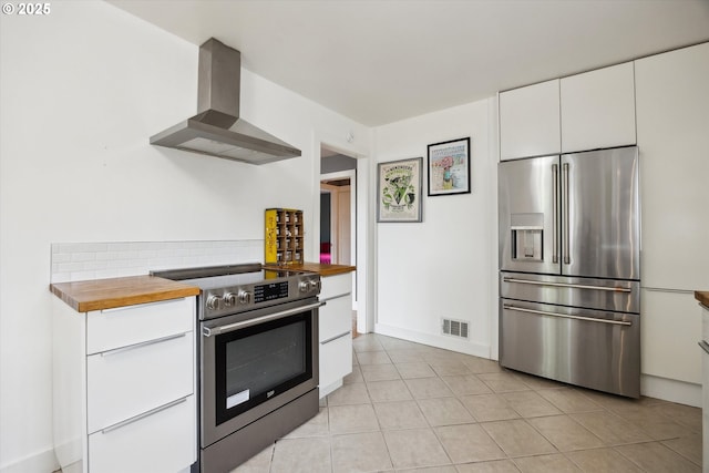 kitchen featuring appliances with stainless steel finishes, wall chimney range hood, white cabinetry, wood counters, and light tile patterned floors