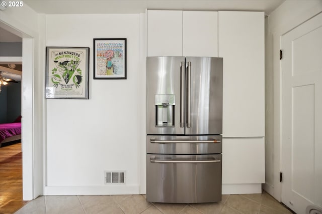 kitchen featuring stainless steel fridge, white cabinets, and light tile patterned flooring