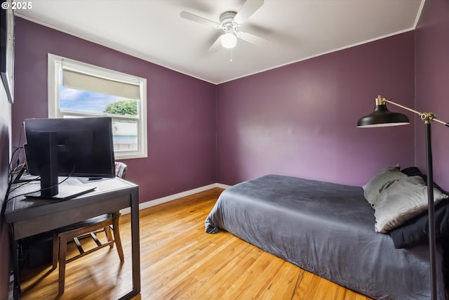 bedroom with baseboards, wood finished floors, an office area, a ceiling fan, and ornamental molding