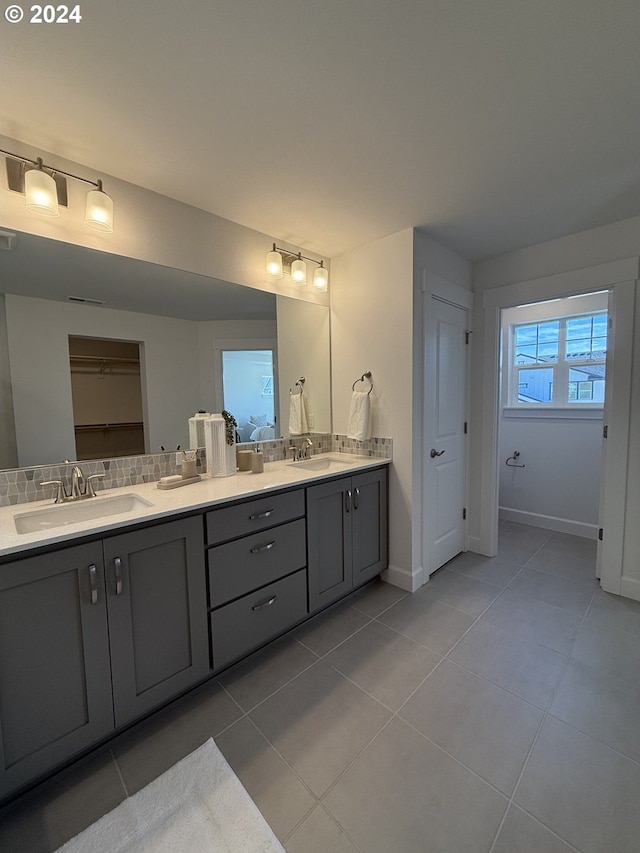 bathroom featuring tile patterned floors, backsplash, a sink, baseboards, and double vanity