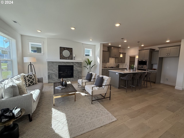 living room with a premium fireplace, light wood-type flooring, baseboards, visible vents, and recessed lighting