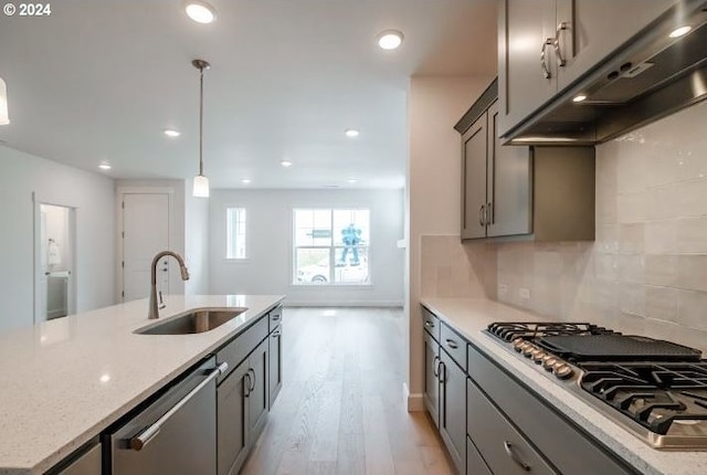 kitchen featuring light stone counters, extractor fan, stainless steel appliances, a sink, and hanging light fixtures