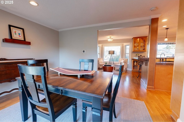 dining space featuring sink, ornamental molding, and light hardwood / wood-style flooring