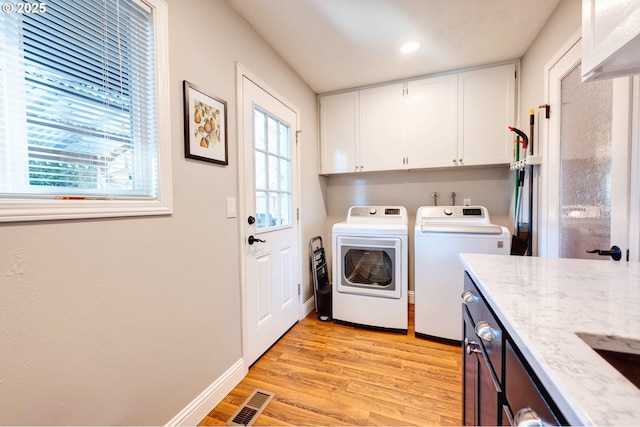 clothes washing area featuring cabinets, separate washer and dryer, a healthy amount of sunlight, and light hardwood / wood-style flooring