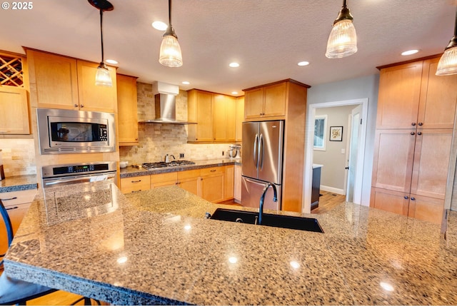 kitchen with appliances with stainless steel finishes, wall chimney exhaust hood, light stone countertops, decorative backsplash, and pendant lighting