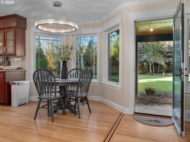 dining space with ornamental molding, plenty of natural light, light wood-type flooring, and an inviting chandelier