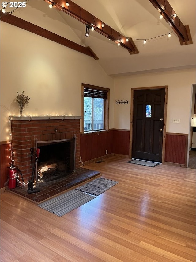 unfurnished living room with light wood-type flooring, a brick fireplace, vaulted ceiling with beams, and wooden walls