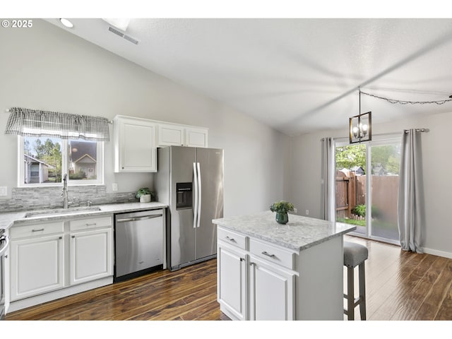 kitchen with a sink, vaulted ceiling, stainless steel appliances, and dark wood-style floors