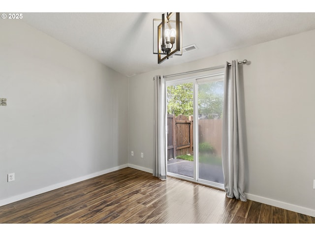 spare room featuring dark wood-style flooring, baseboards, visible vents, and an inviting chandelier