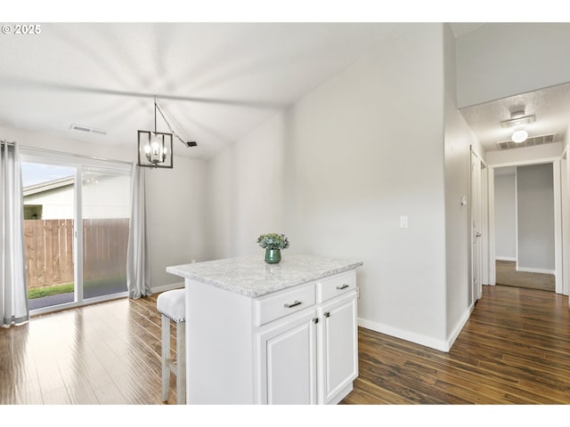 kitchen with visible vents, a kitchen island, baseboards, dark wood-type flooring, and white cabinets