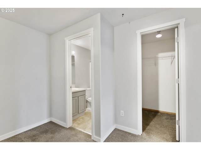 unfurnished bedroom with a closet, carpet flooring, baseboards, and ensuite bath
