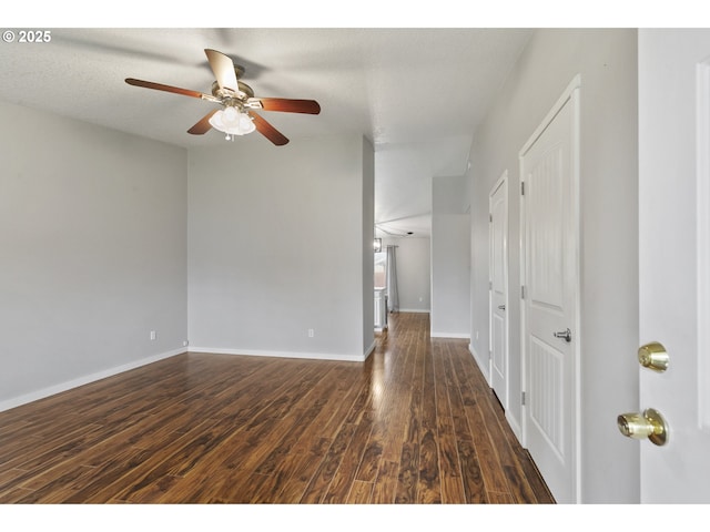 empty room featuring dark wood-type flooring, a ceiling fan, and baseboards