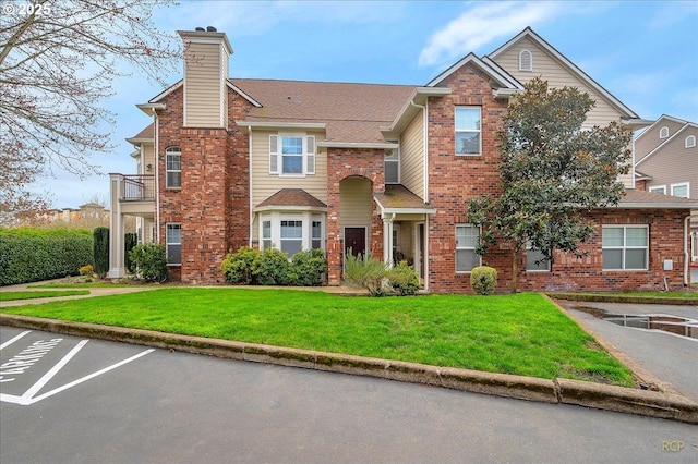 multi unit property featuring a front lawn, uncovered parking, brick siding, and a chimney