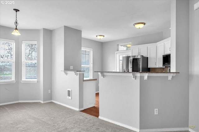 kitchen featuring dark stone countertops, a kitchen breakfast bar, fridge, carpet floors, and white cabinets