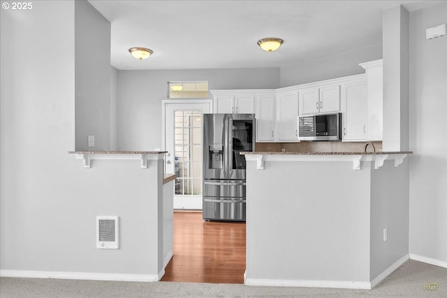 kitchen featuring a kitchen bar, stone counters, a peninsula, stainless steel appliances, and white cabinetry