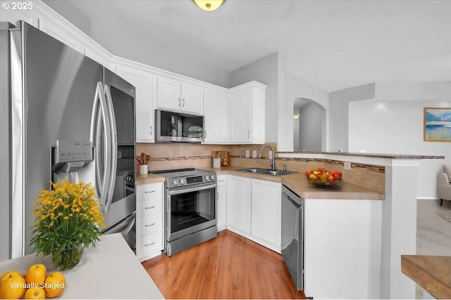 kitchen with a sink, tasteful backsplash, stainless steel appliances, a peninsula, and light countertops