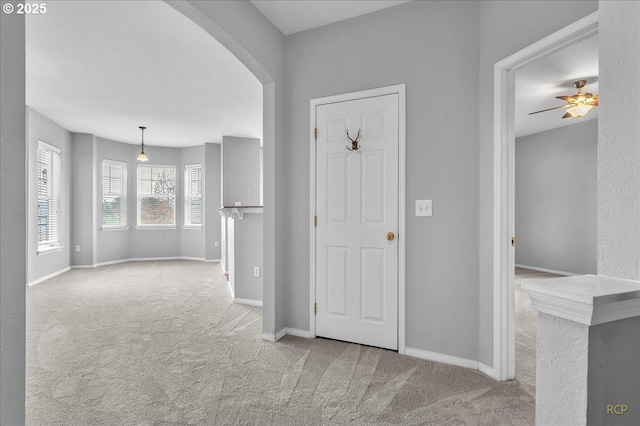 carpeted entrance foyer with baseboards, arched walkways, and a ceiling fan