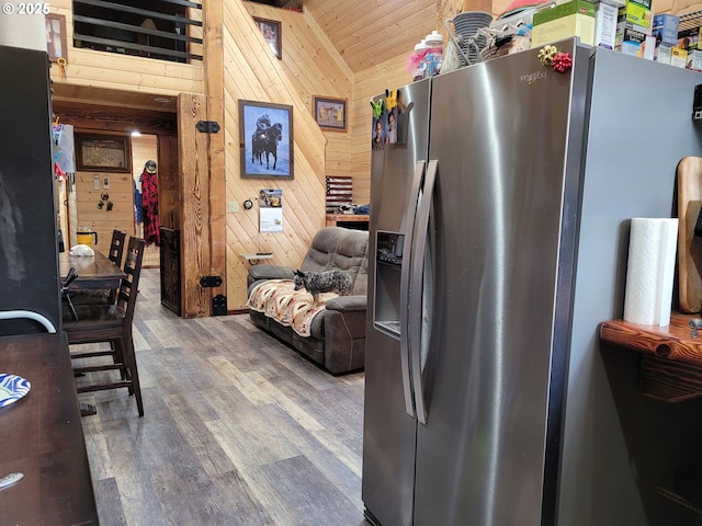kitchen with vaulted ceiling, wood walls, wood finished floors, open floor plan, and stainless steel fridge