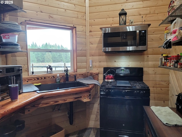 kitchen featuring wooden walls, black range with gas cooktop, and stainless steel microwave