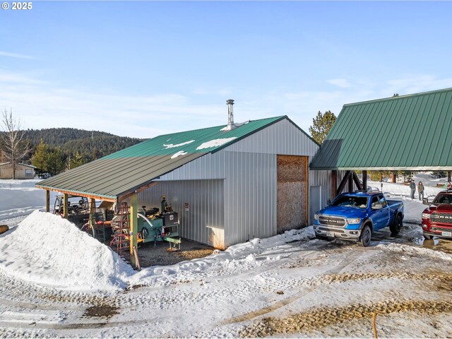 snow covered structure featuring a detached carport, an outbuilding, and an outdoor structure