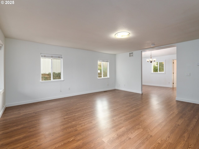 spare room with a notable chandelier and dark hardwood / wood-style floors