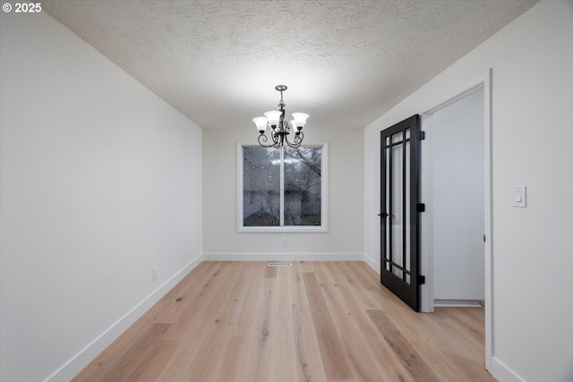 unfurnished dining area with a chandelier, a textured ceiling, and light hardwood / wood-style flooring