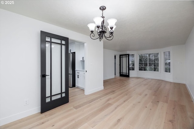 spare room featuring light wood-type flooring and a chandelier