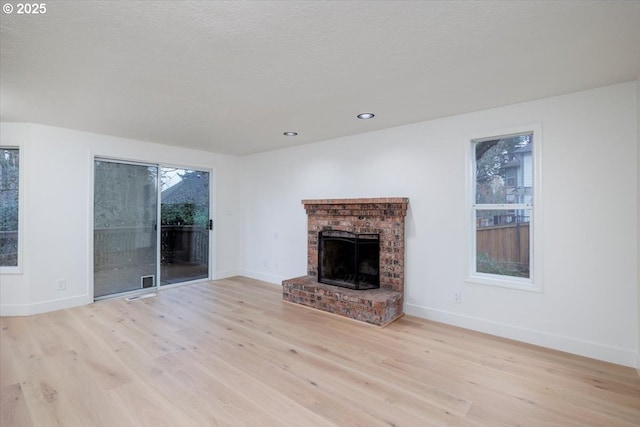 unfurnished living room with light hardwood / wood-style floors, a textured ceiling, and a brick fireplace