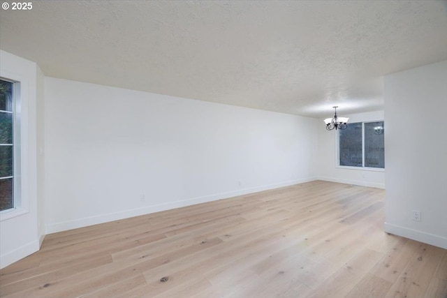 unfurnished room featuring a notable chandelier, light hardwood / wood-style floors, and a textured ceiling