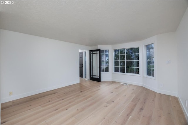 spare room with a textured ceiling and light hardwood / wood-style flooring