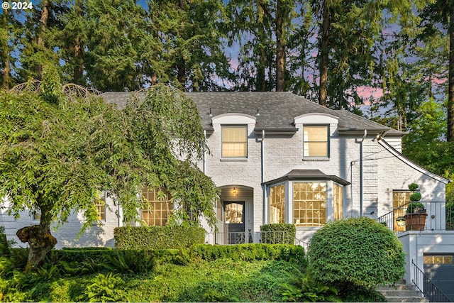 french provincial home with a shingled roof and brick siding