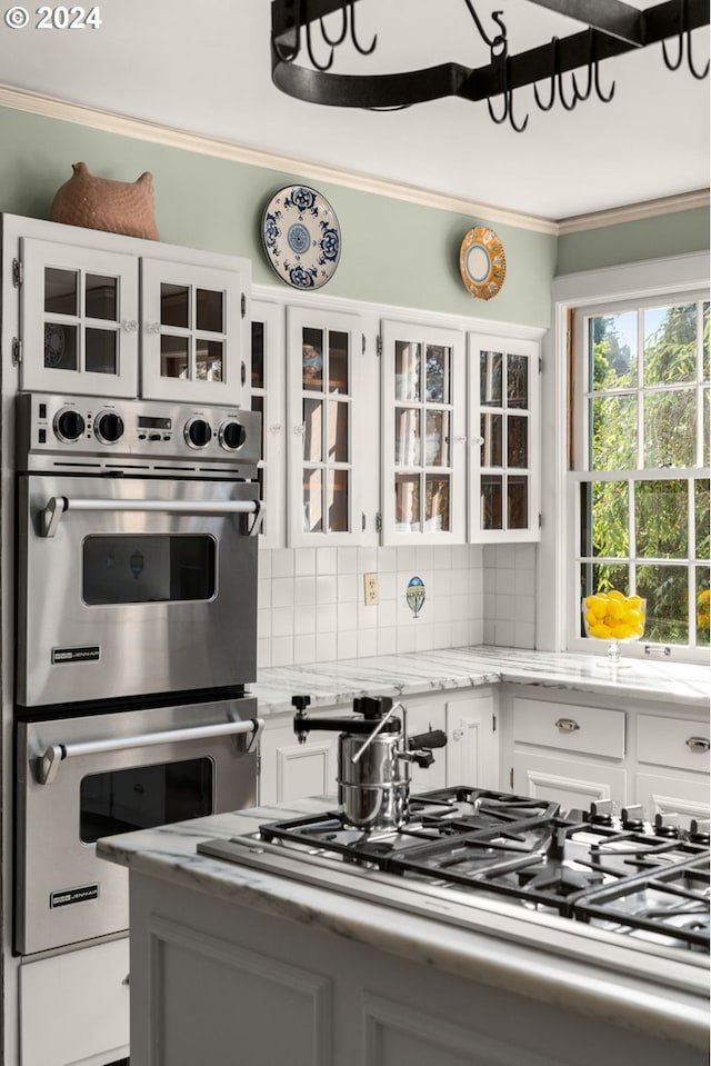 kitchen with appliances with stainless steel finishes, white cabinetry, decorative backsplash, glass insert cabinets, and ornamental molding