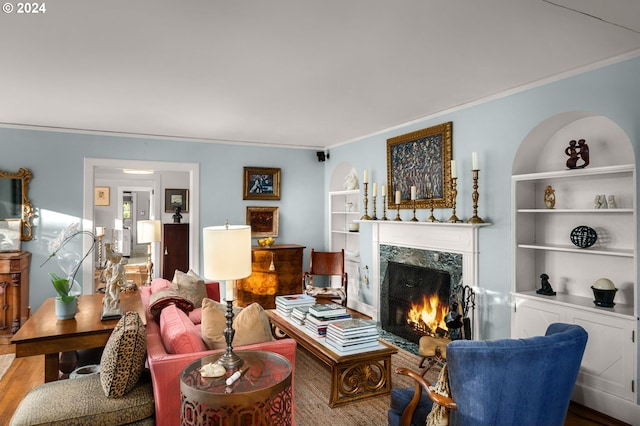 living area featuring ornamental molding, a high end fireplace, wood finished floors, and built in features