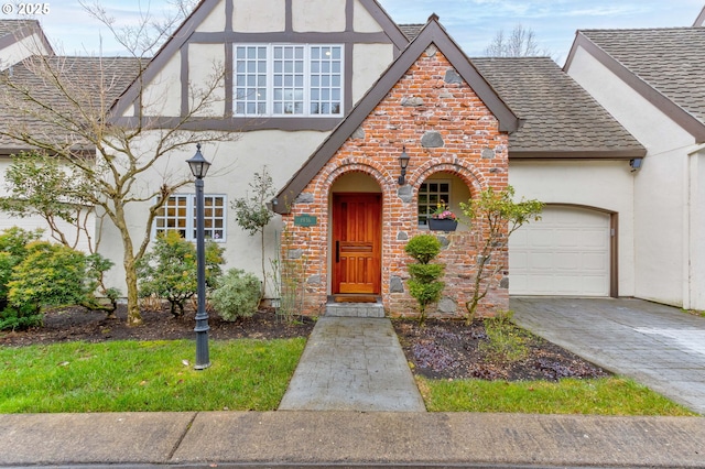 tudor-style house with driveway, brick siding, an attached garage, and stucco siding