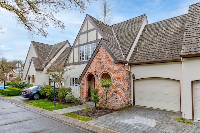 view of front facade featuring a garage, decorative driveway, brick siding, and stucco siding