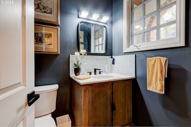 bathroom with a textured wall, vanity, toilet, and decorative backsplash