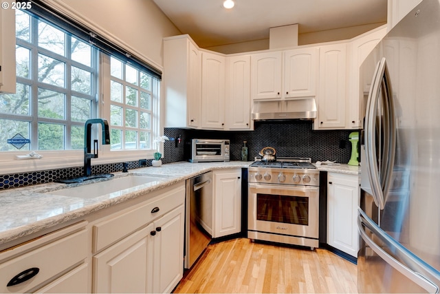 kitchen featuring decorative backsplash, stainless steel appliances, under cabinet range hood, white cabinetry, and a sink