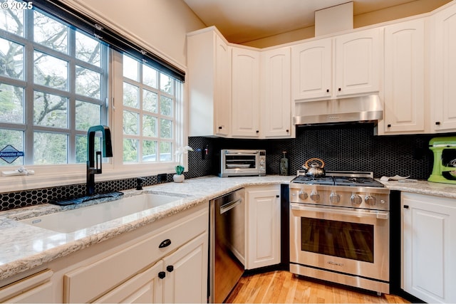 kitchen featuring extractor fan, stainless steel appliances, a sink, white cabinets, and tasteful backsplash