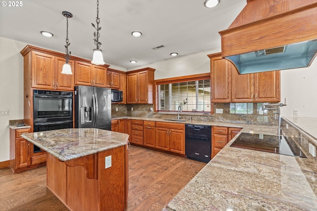 kitchen featuring light stone countertops, black appliances, a sink, and hanging light fixtures